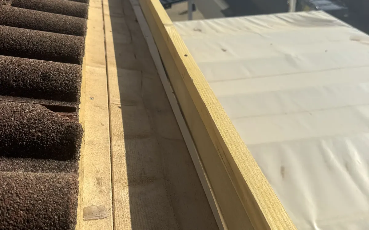 Structure en bois en bordure d’un toit de tuiles canal, à côté d’une toiture recouverte d’une membrane claire