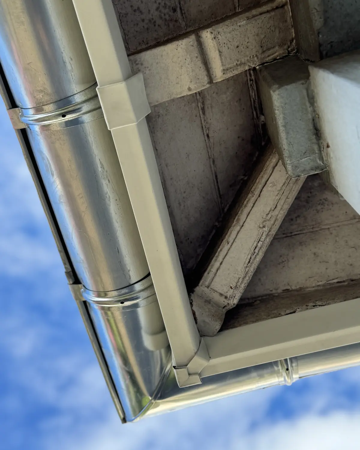 Gouttière et descente en zinc vues d'en dessous, sous un ciel bleu