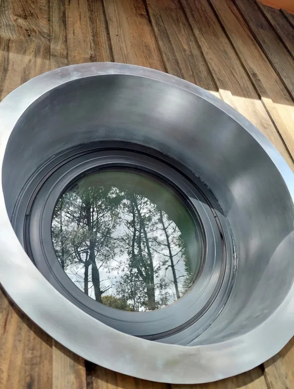 Fenêtre ronde entourée d’une large bordure métallique, sur une façade en planches de bois