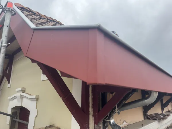 Bandeau rouge bordeaux au bord d’un toit, avec angles pliés et descente métallique coudée