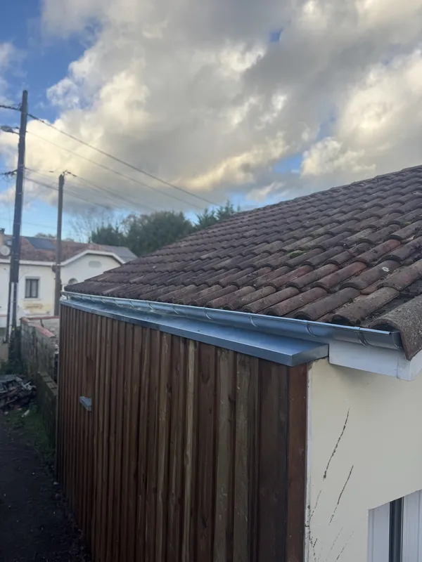 Façade en planches de bois verticales surmontée d’une gouttière demi-ronde et d’une bande de rive métalliques