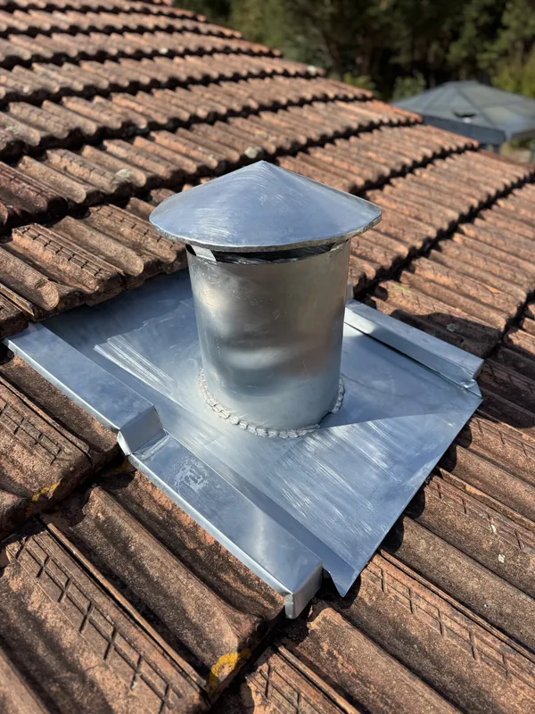 Conduit cylindrique à chapeau conique posé sur une platine métallique, au milieu de tuiles anciennes
