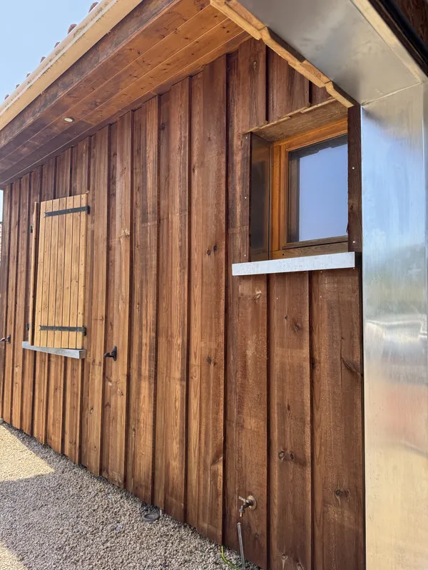 Façade en planches de bois verticales à larges couvre-joints, avec une petite fenêtre à appui métallique
